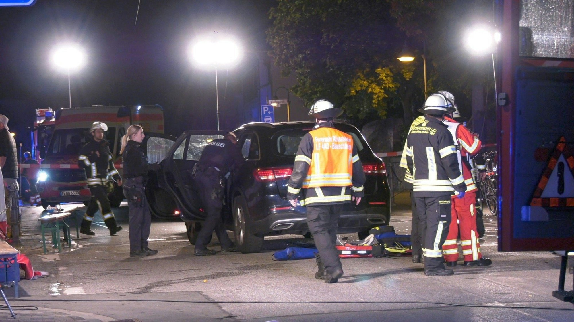 24.09.2022, Hessen, Rüsselsheim: Einsatzkräfte der Polizei und Feuerwehr, sowie Rettungskräfte stehen im Rüsselsheimer Ortsteil Bauschheim an einer Unfallstelle. Ein 49 Jahre alter Mann ist mit seinem Wagen in eine auf der Straße stehende Gruppe Feiernder gefahren.