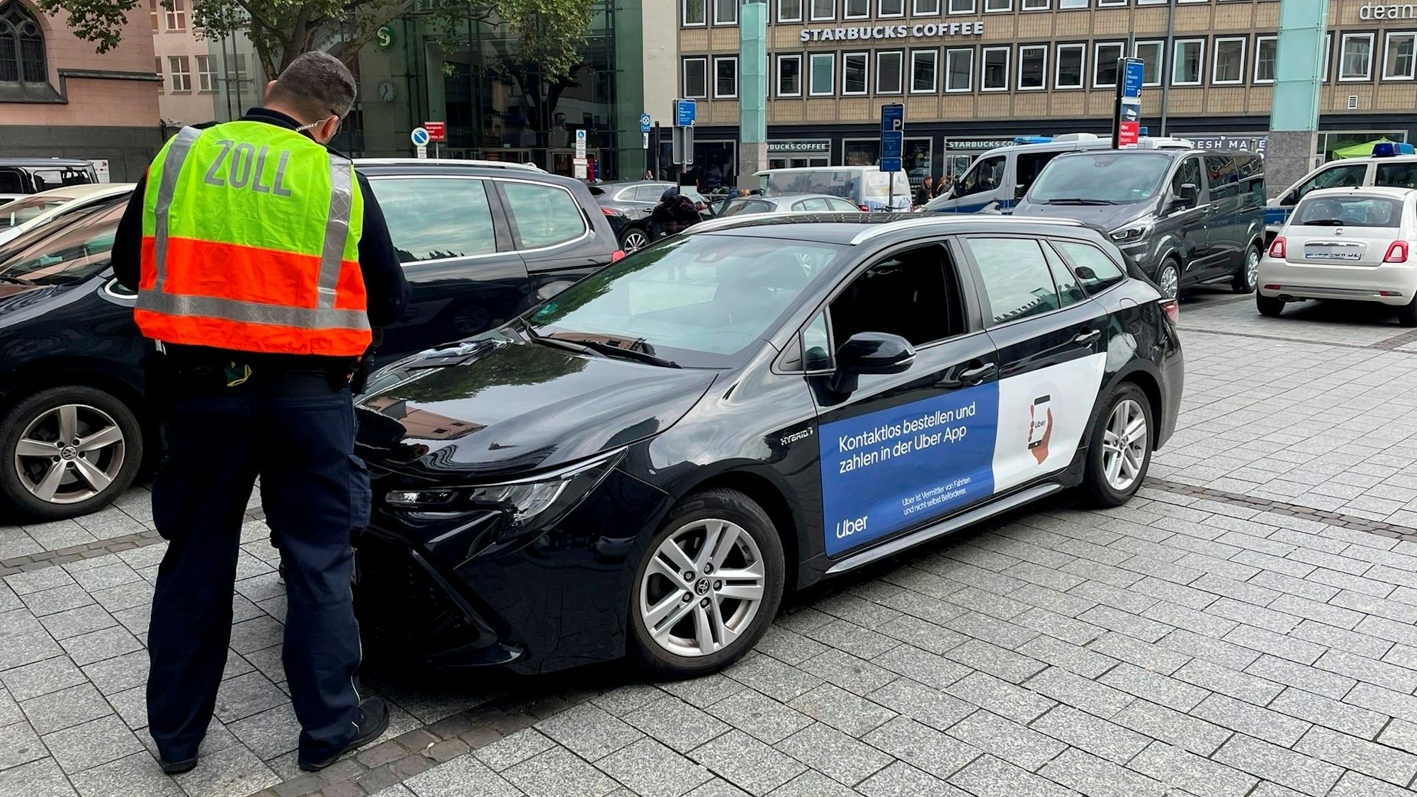Ein Zollbeamter steht vor einem Fahrzeug, an dessen Seite Werbung für Uber klebt.