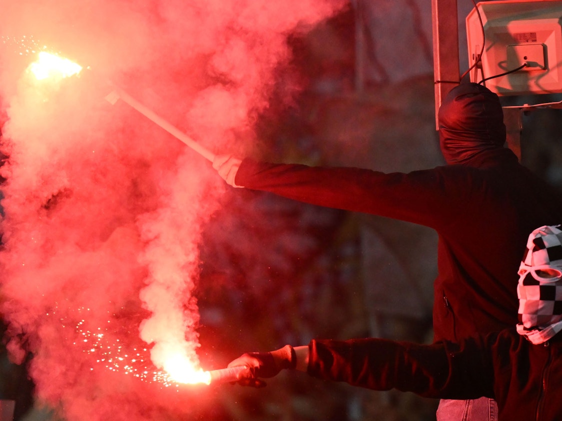 Zwei vermummte Fußballfans zünden Bengalos.