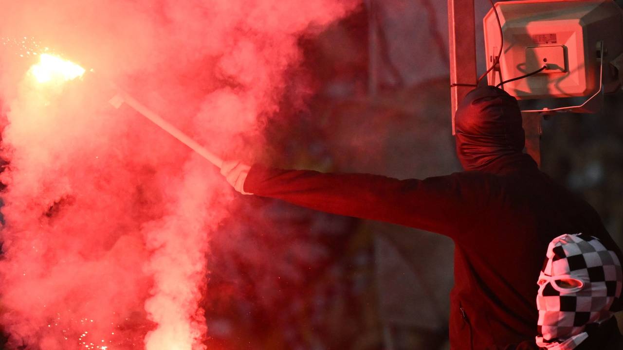 Zwei vermummte Fußballfans zünden Bengalos.