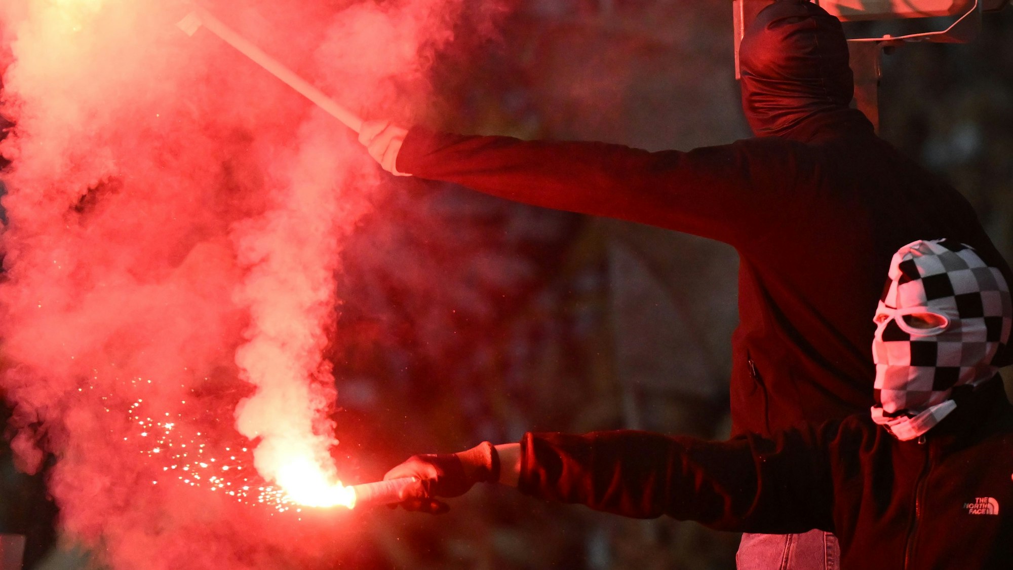 Zwei vermummte Fußballfans zünden Bengalos.