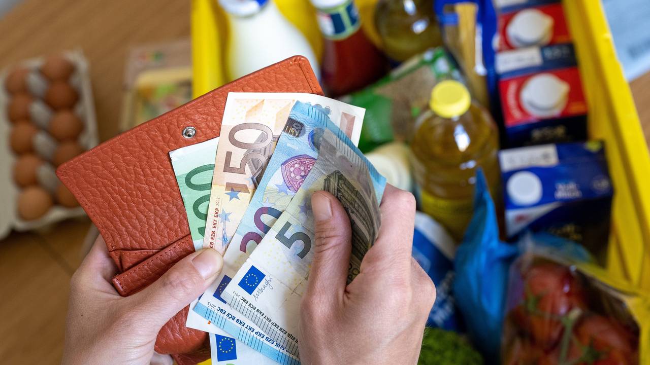 Eine Einkaufskiste mit Lebensmitteln steht auf einem Küchentisch, während eine Frau Euro-Banknoten in den Händen hält. Ab Oktober ändert sich einiges, auch finanziell.