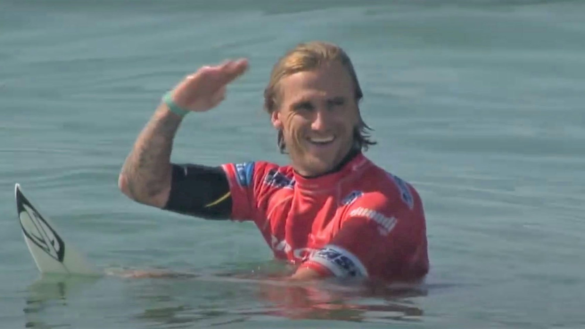 Der australische Surfer Chris Davidson grüßt bei einem Wettkampf auf der Pro Tour in Portugal auf seinem Surfboard sitzend das Publikum.