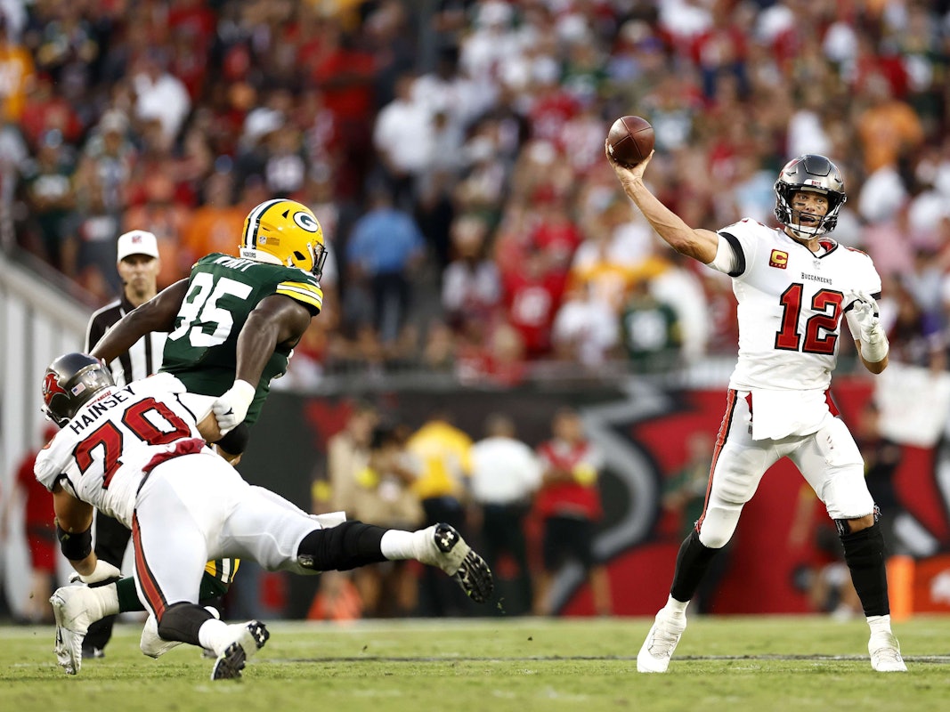 Tom Brady (r.) wirft einen Football, während ein Gegenspieler der Green Bay Packers versucht, ihn daran zu hindern.