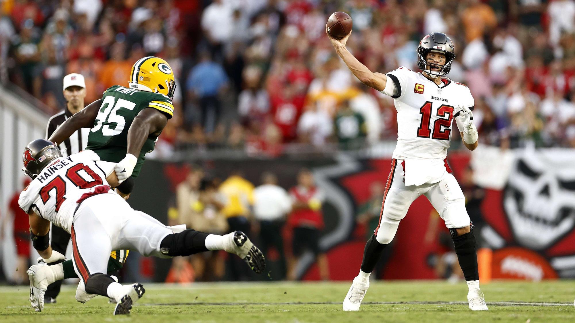Tom Brady (r.) wirft einen Football, während ein Gegenspieler der Green Bay Packers versucht, ihn daran zu hindern.