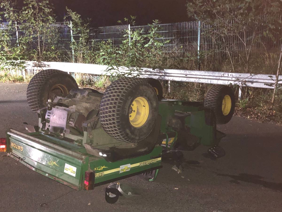 Ein Arbeitsfahrzeug mit offener Ladefläche hat sich überschlagen und liegt mit den Rädern nach oben auf der Straße.