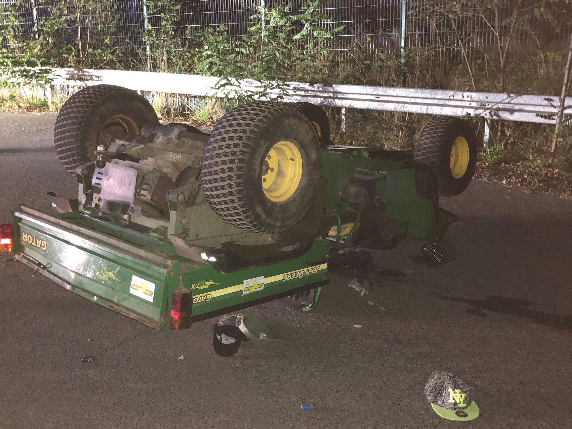 Ein Arbeitsfahrzeug mit offener Ladefläche hat sich überschlagen und liegt mit den Rädern nach oben auf der Straße.