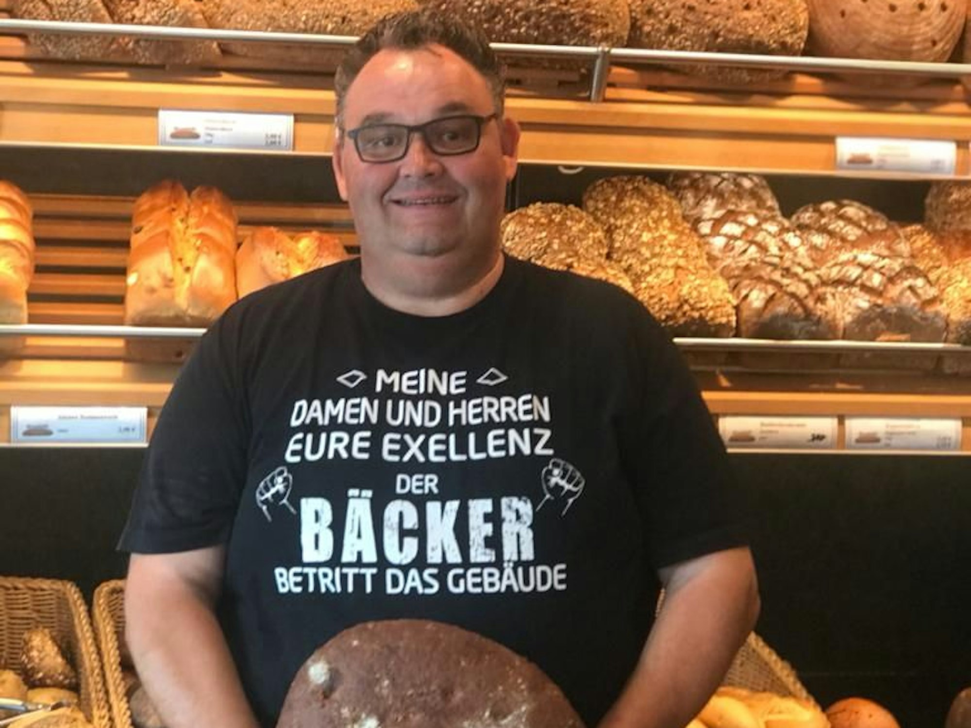Bäcker Gudio Boveleth steht in seiner Bäckerei vor einem Brotregal.