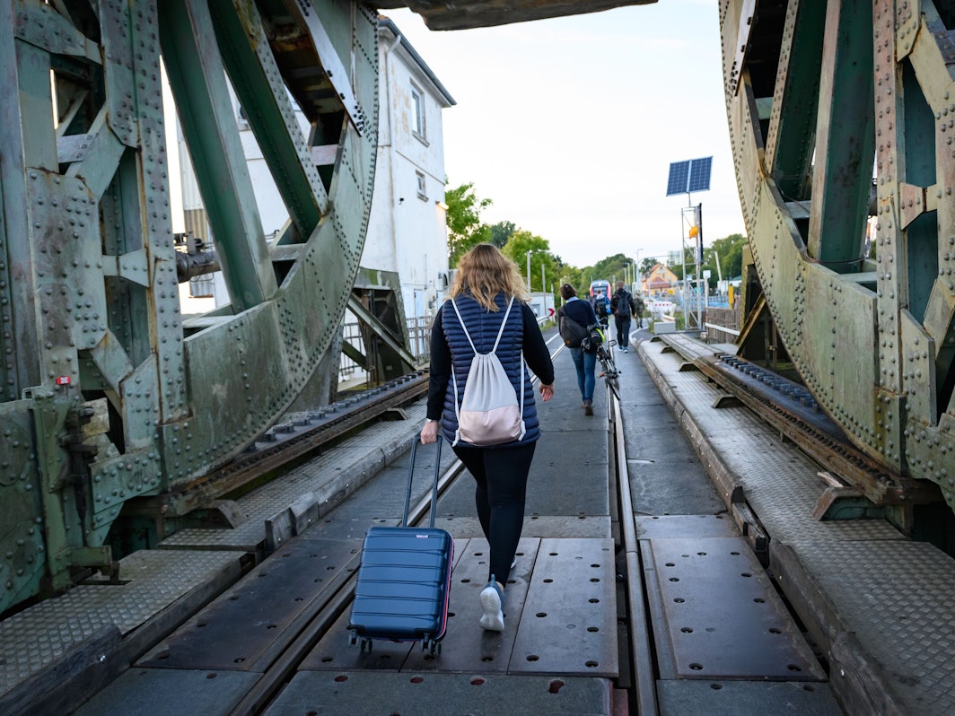 Eine Frau läuft mit einem Koffer über die Lindaunisbrücke. Normalerweise fahren Züge über die Schleibrücke bei Lindaunis. Seit Mitte September aber heißt es für Fahrgäste: Austeigen und zu Fuß die Schlei passieren.