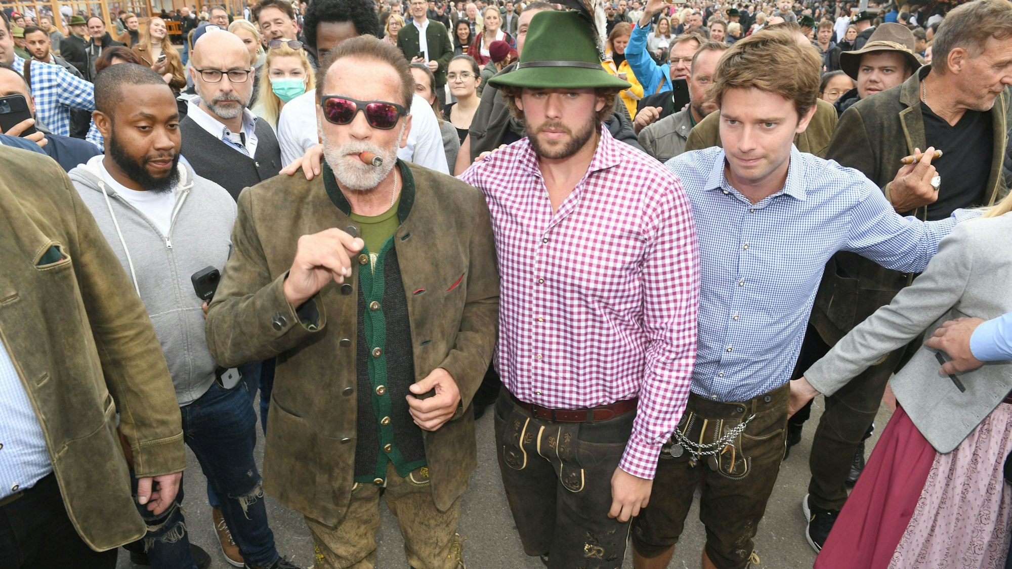 Schauspieler Arnold Schwarzenegger zusammen mit seinen Söhnen Christopher Schwarzenegger und Patrick Schwarzenegger auf dem Oktoberfest. Alle Schwarzeneggers tragen Tracht. Arnold raucht genüsslich eine Zigarre.