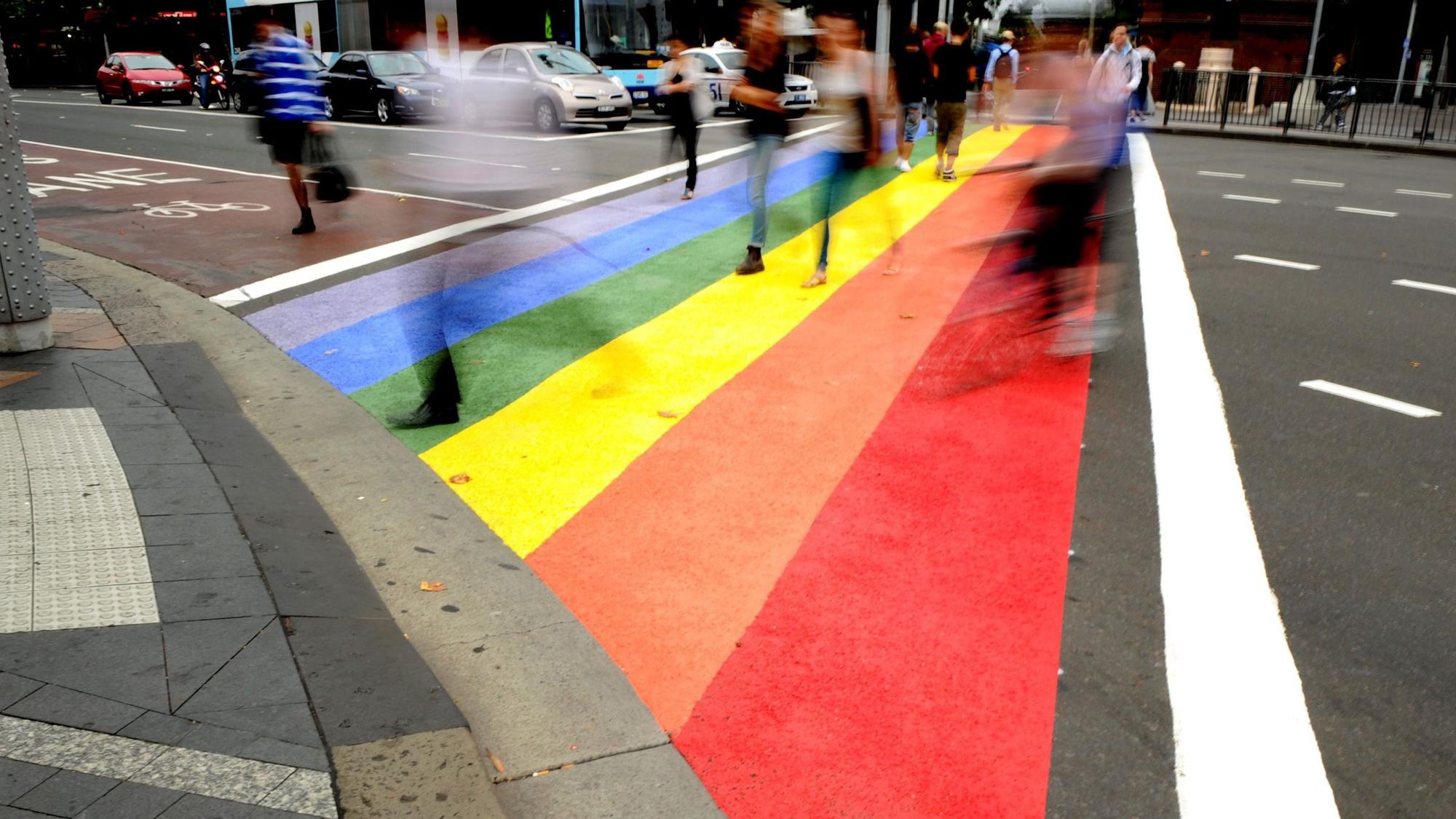 Menschen gehen über einen Zebrastreifen in den Farben des Regenbogens.
