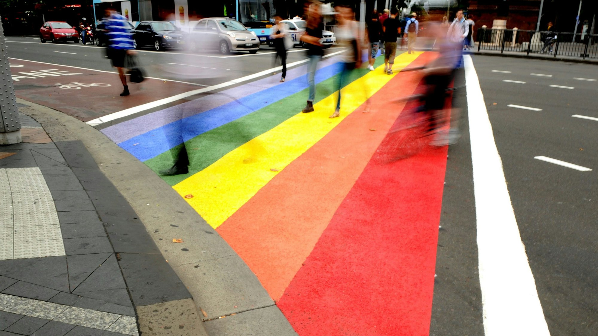Menschen gehen über einen Zebrastreifen in den Farben des Regenbogens.