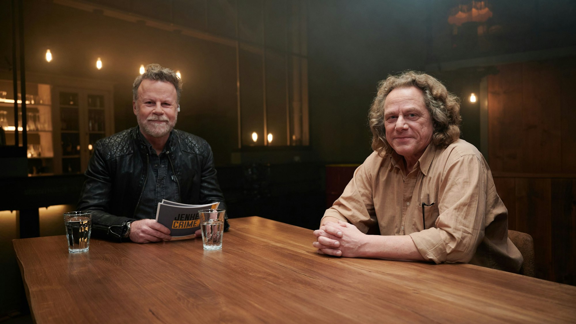 Jenke von Wilmsdorff (l.)und Dieter Gurkasch (r.) sitzen an einem Tisch. Sie schauen in die Kamera.