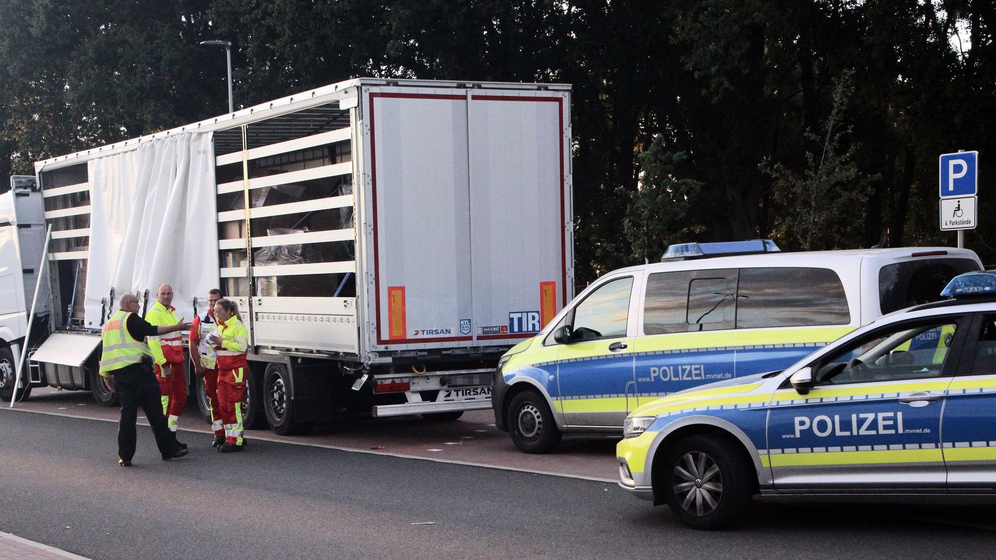 Ein Polizist und Mitarbeiter des Rettungsdienstes diskutieren vor einem Sattelauflieger.