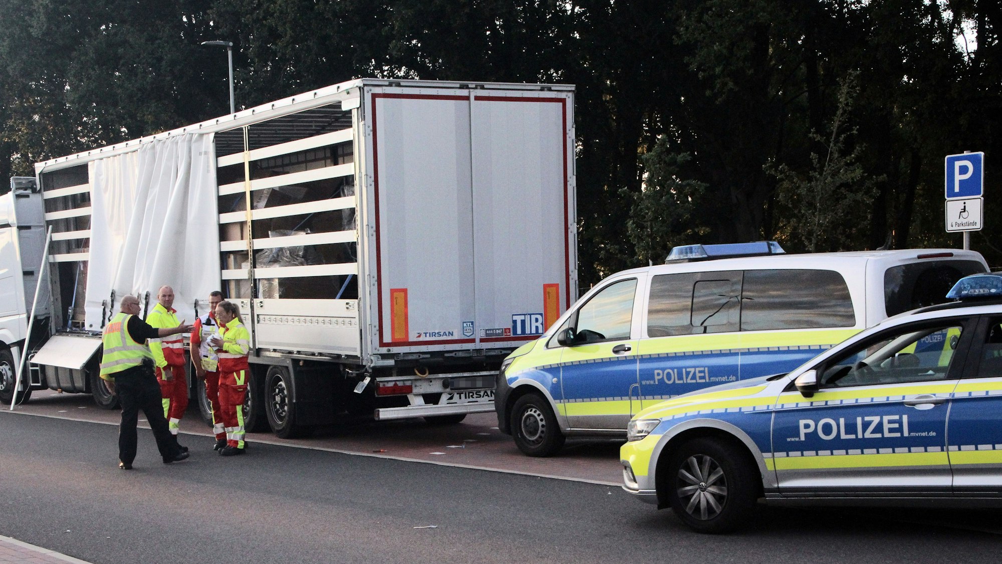 Ein Polizist und Mitarbeiter des Rettungsdienstes diskutieren vor einem Sattelauflieger.