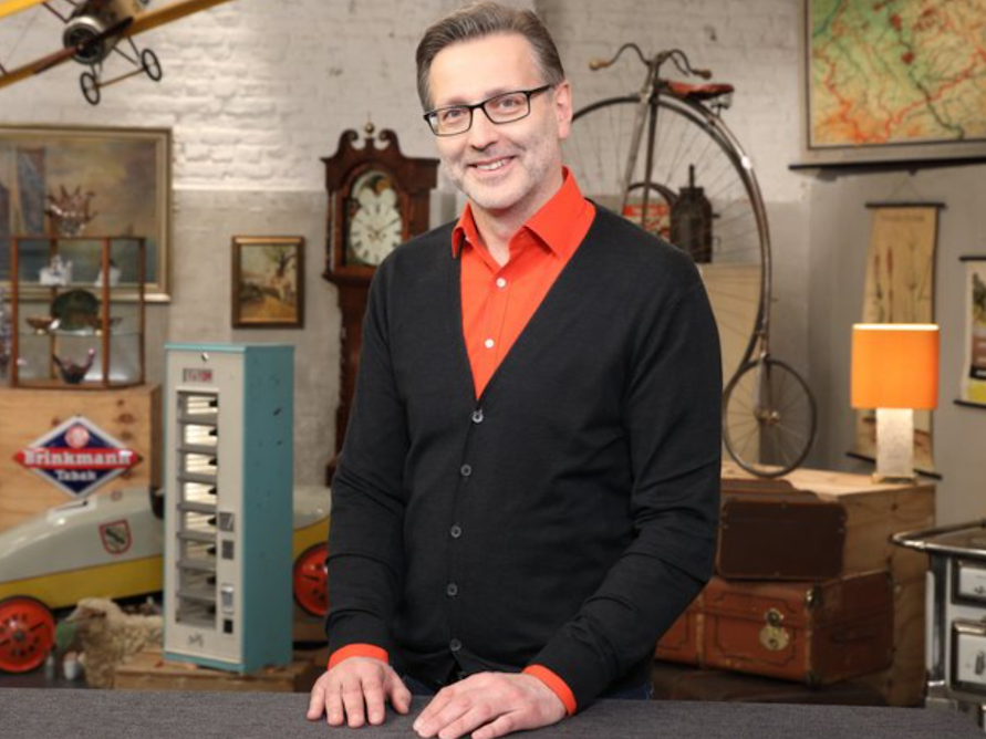 Experte Detlev posiert in einem orangen Hemd und schwarzer Strickjacke für die Kamera.