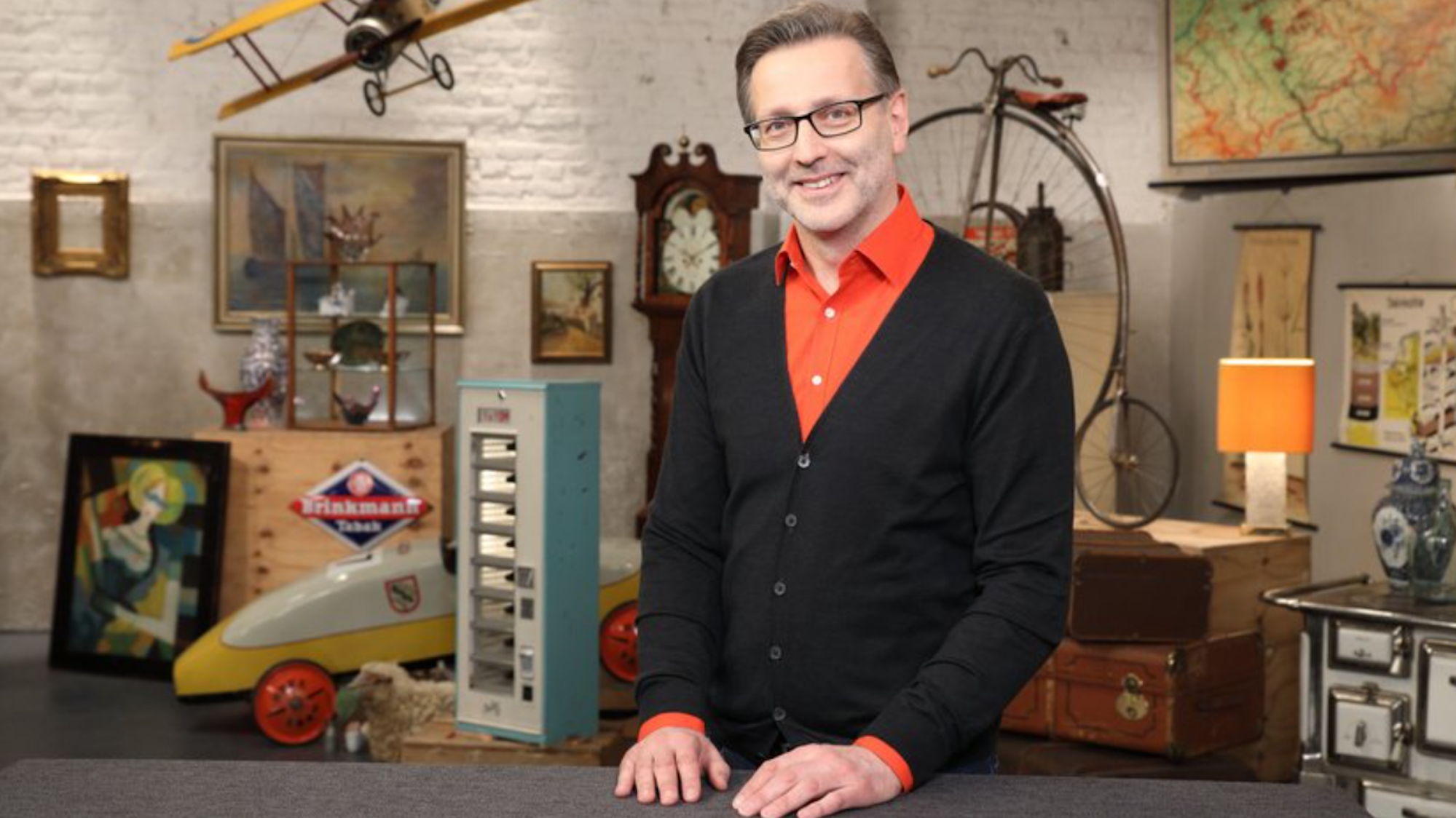 Experte Detlev posiert in einem orangen Hemd und schwarzer Strickjacke für die Kamera.