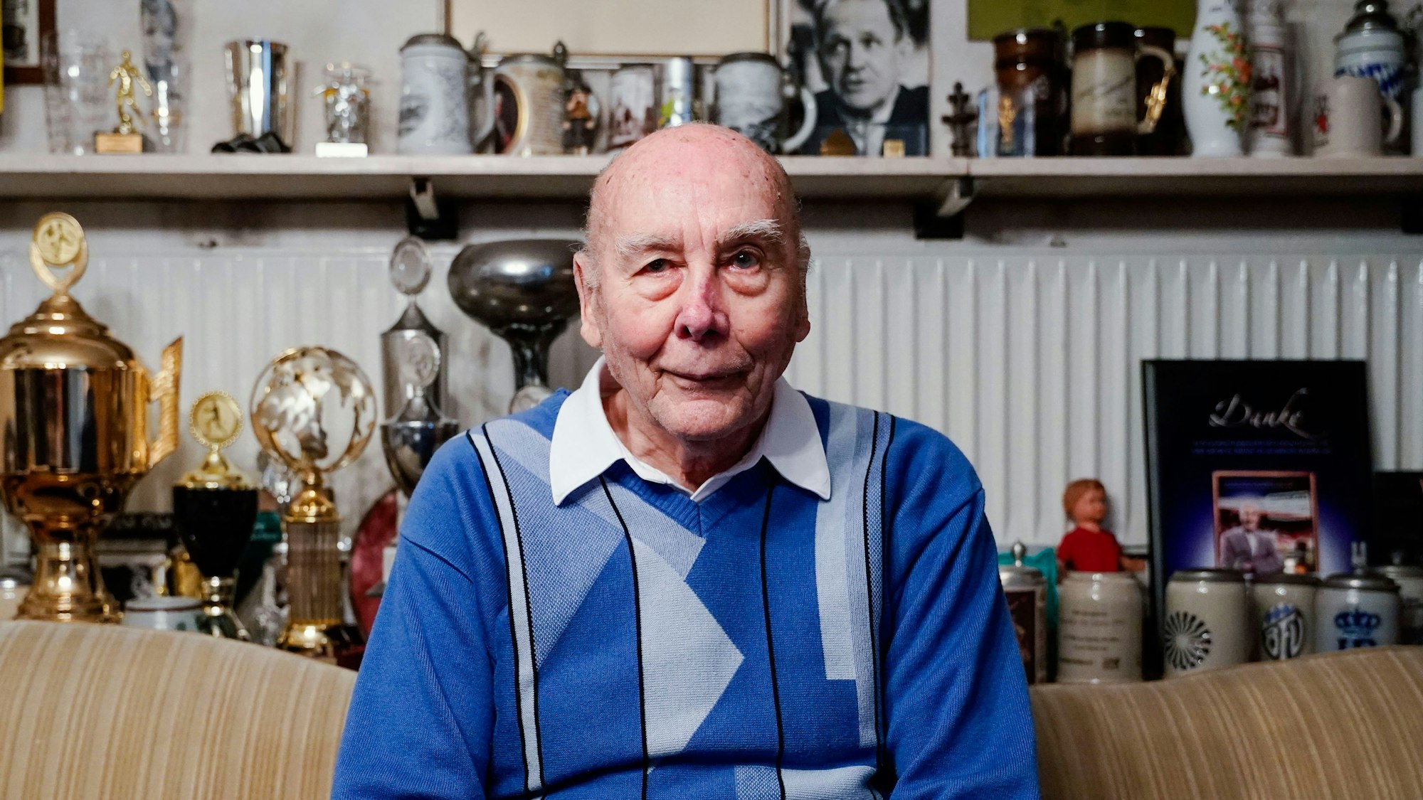 Der ehemalige Fussballspieler Horst Eckel sitzt in seinem Haus vor einem Regal mit Pokalen und weiteren Erinnerungen.