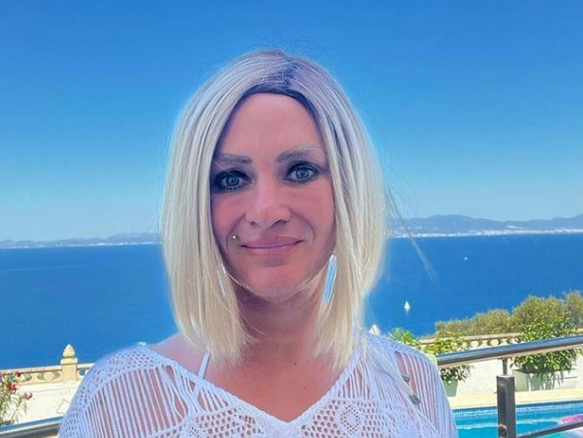 Caro Robens blickt in einem weißen Sommerkleid in die Kamera. Hinter ihr befindet sich das Mittelmeer.