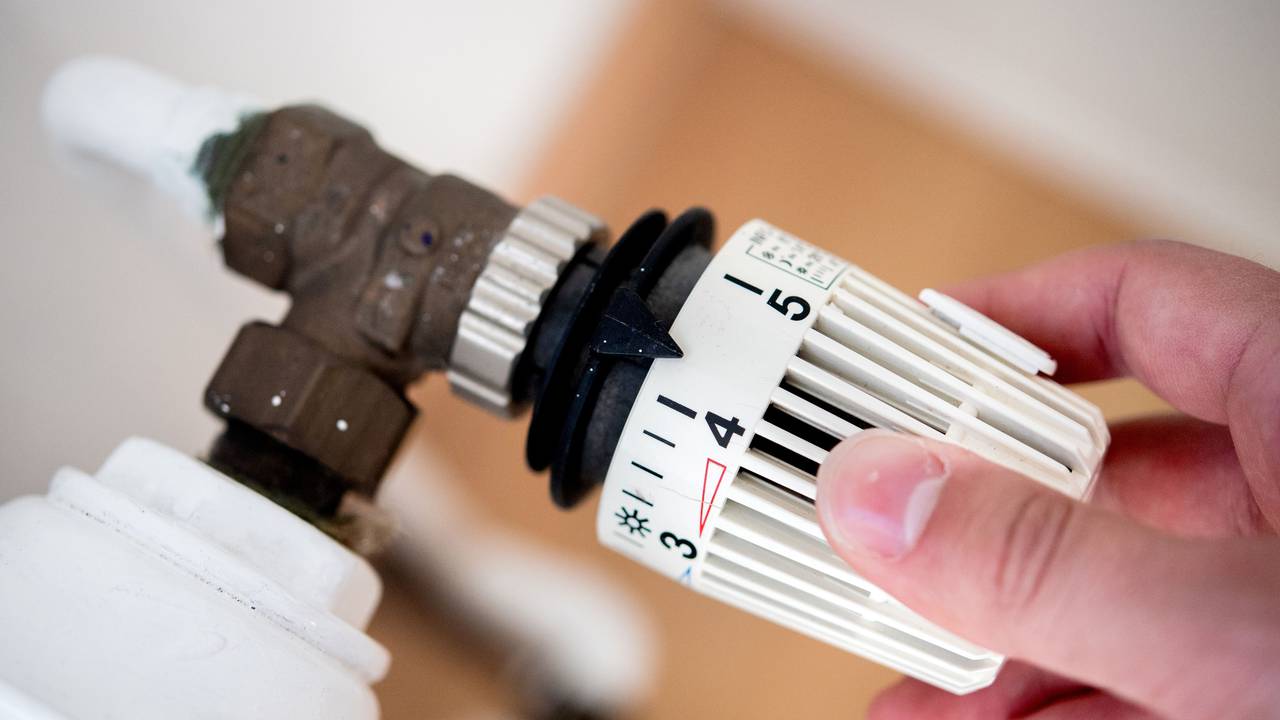 Ein Mann dreht in einer Wohnung am Thermostat einer Heizung, bei der Aufnahme handelt es sich um ein Symbolfoto.