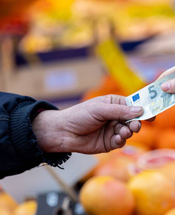 Ein Kunde bezahlt seinen Einkauf an einem Stand auf einem Wochenmarkt mit einem Fünf-Euro-Schein.