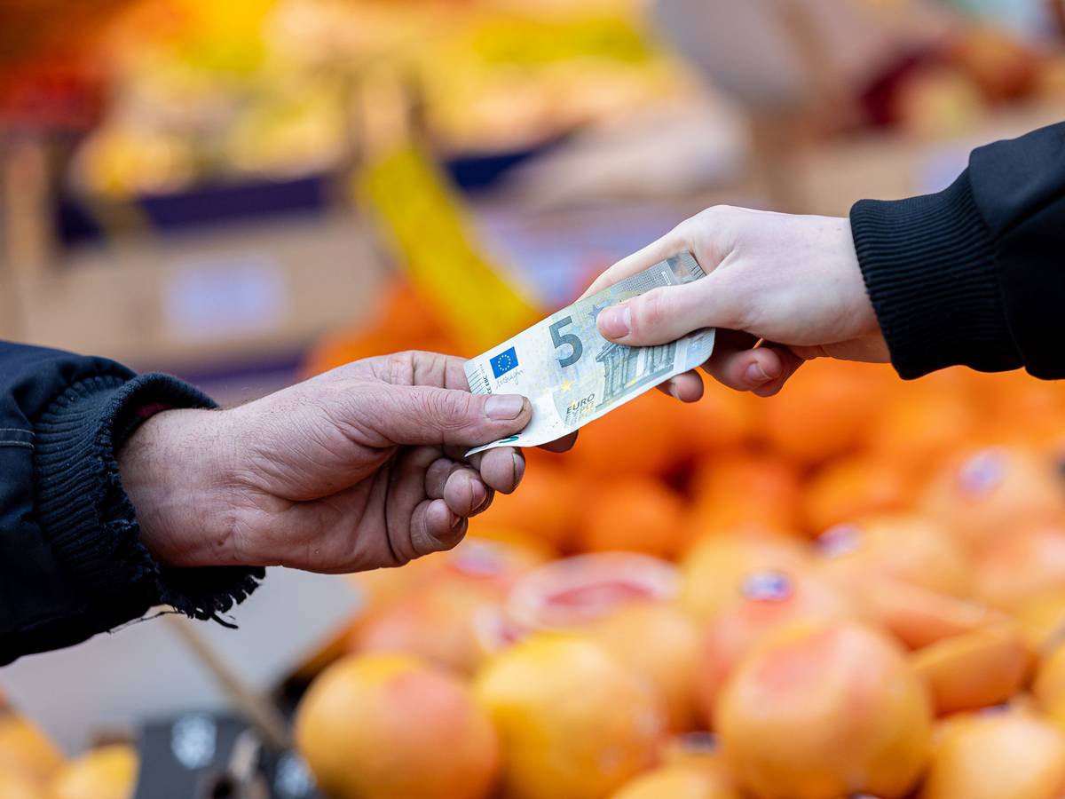 Ein Kunde bezahlt seinen Einkauf an einem Stand auf einem Wochenmarkt mit einem Fünf-Euro-Schein.