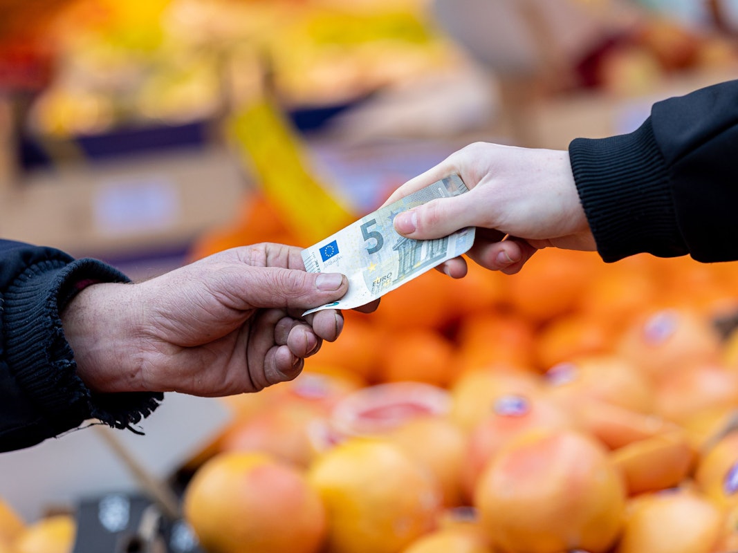 Ein Kunde bezahlt seinen Einkauf an einem Stand auf einem Wochenmarkt mit einem Fünf-Euro-Schein.