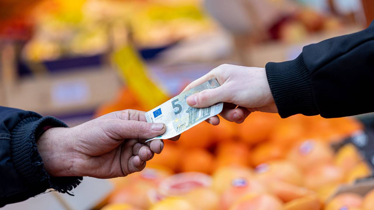 Ein Kunde bezahlt seinen Einkauf an einem Stand auf einem Wochenmarkt mit einem Fünf-Euro-Schein.