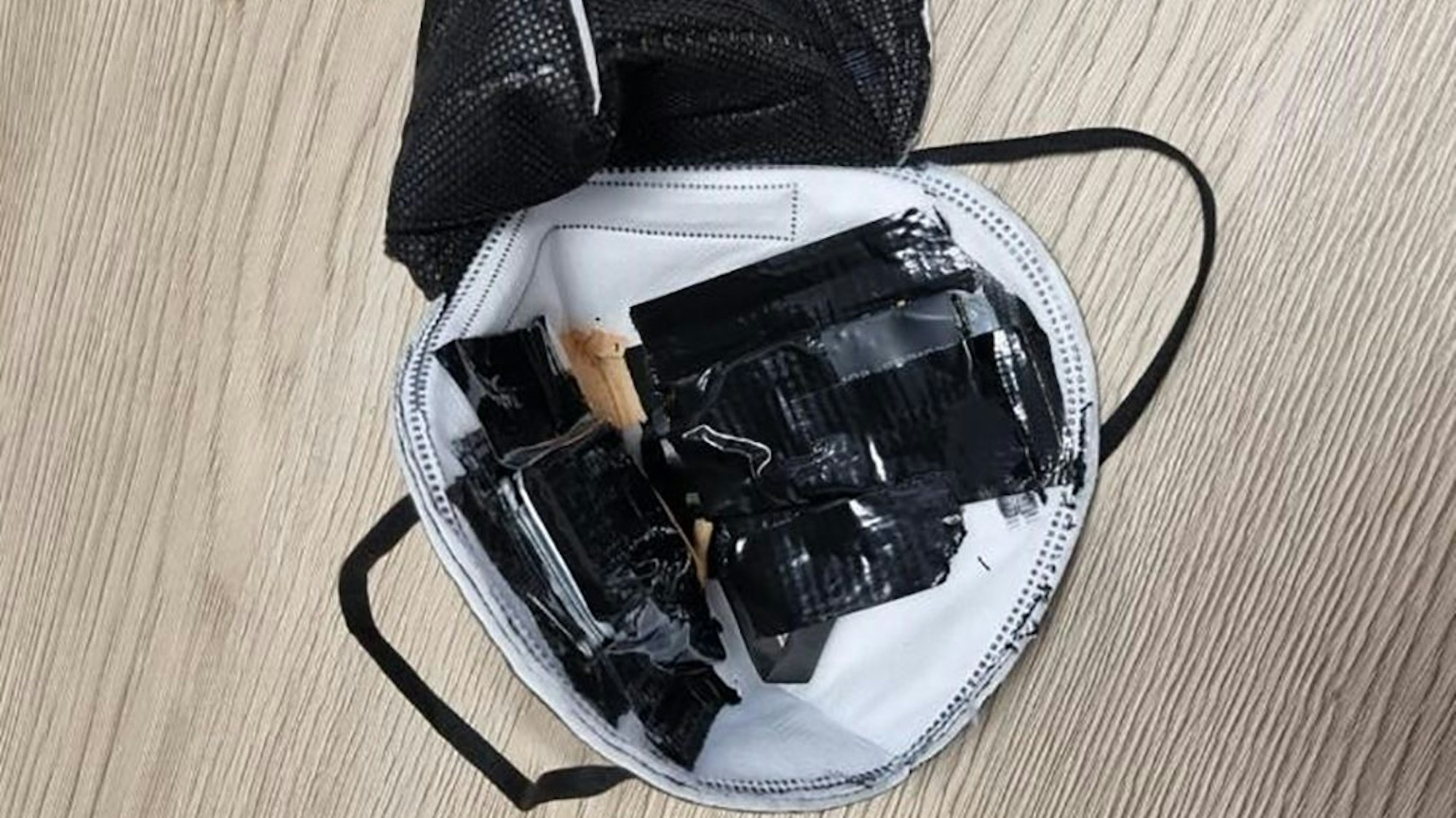 Eine eingenähte Kamera in einer FFP2-Maske liegt auf einem Tisch des TÜV Süd (undatierte Aufnahme). Sie war bei einer theoretischen Führerscheinprüfung entdeckt worden. Einen ähnlichen Betrugsfall gab es jetzt in Bergheim.