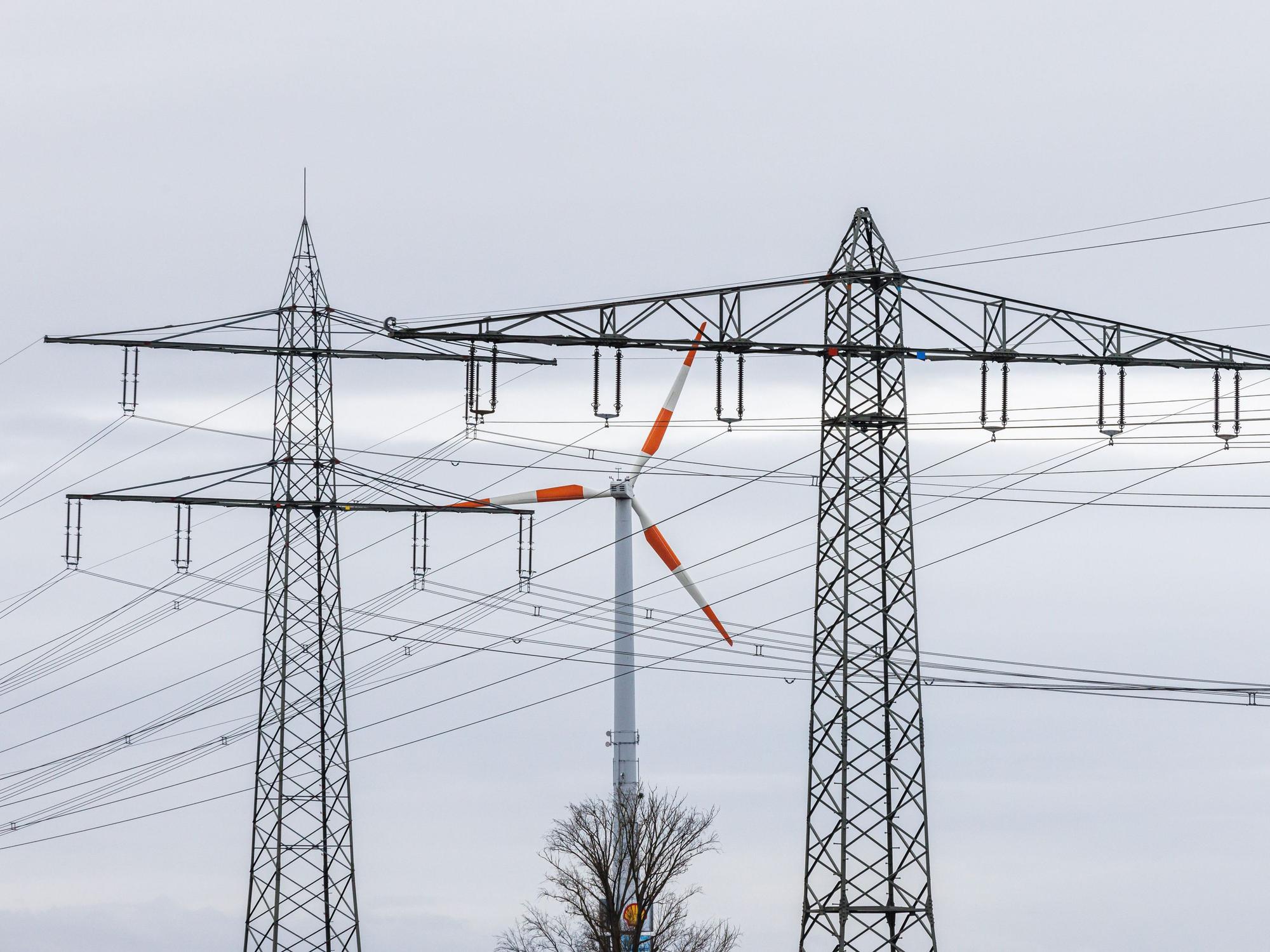 Ein Windrad steht neben dem Mast einer Hochspannungsleitung und dreht sich im Wind. Die Energieminister der EU-Länder haben am Freitag Notfallmaßnahmen gegen die gestiegenen Strompreise beschlossen.