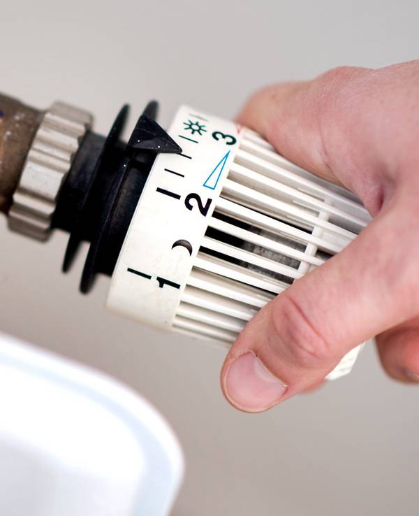 Eine Frau dreht am Thermostat einer Heizung.