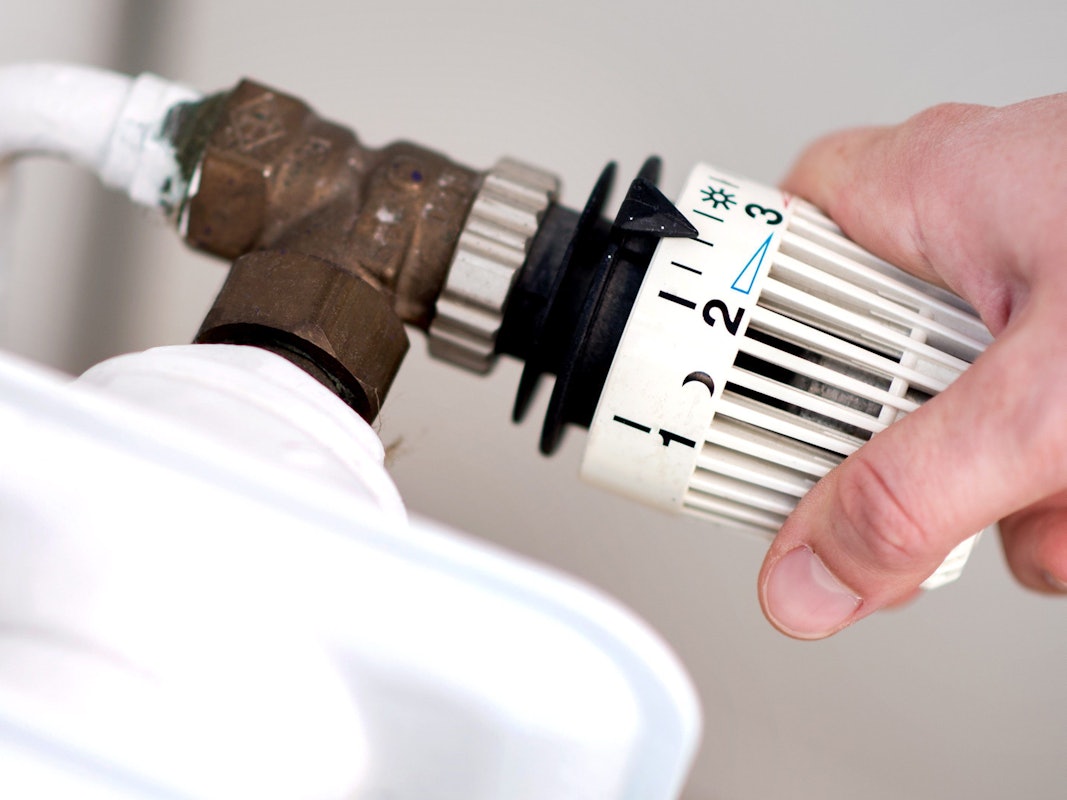 Eine Frau dreht am Thermostat einer Heizung.