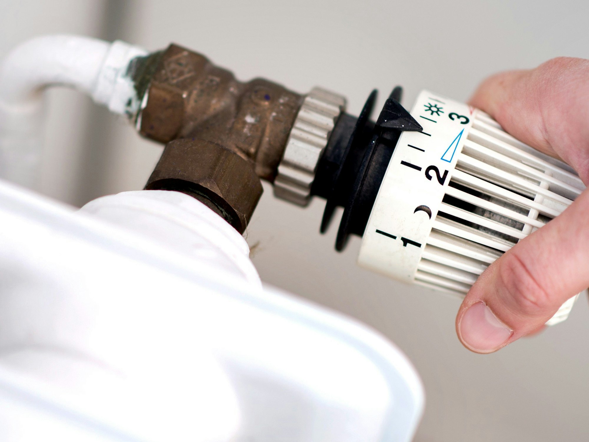 Eine Frau dreht am Thermostat einer Heizung.