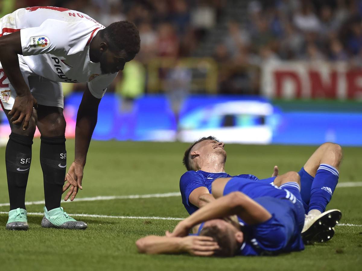 Joris Gnagnon, damals noch im Trikot des FC Sevilla, bückt sich, während zwei Gegenspieler verletzt auf dem Rasen liegen.