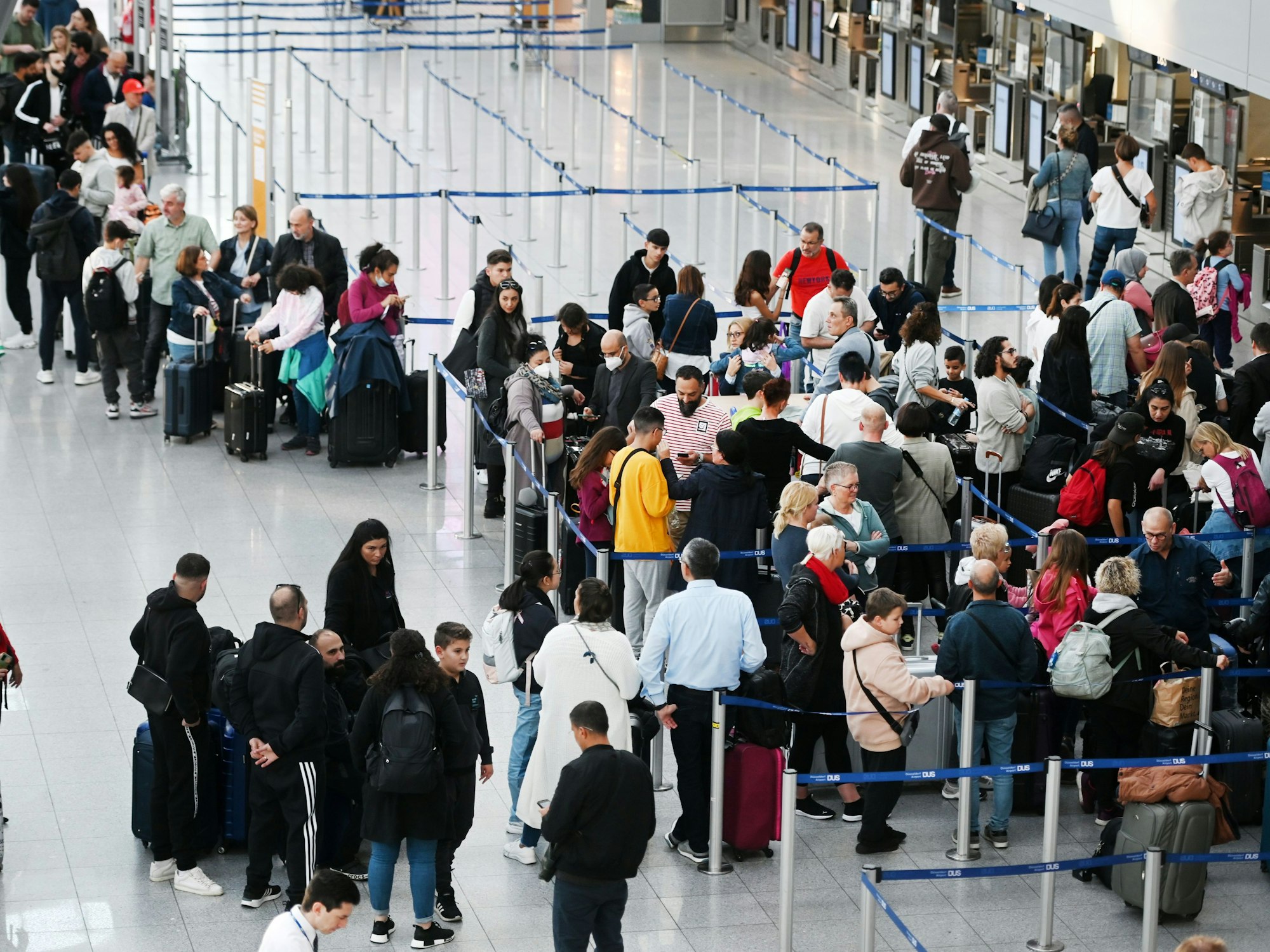 Reisende des Düsseldorfer Flughafens stehen in der Abflugshalle an den Schaltern in Schlangen.