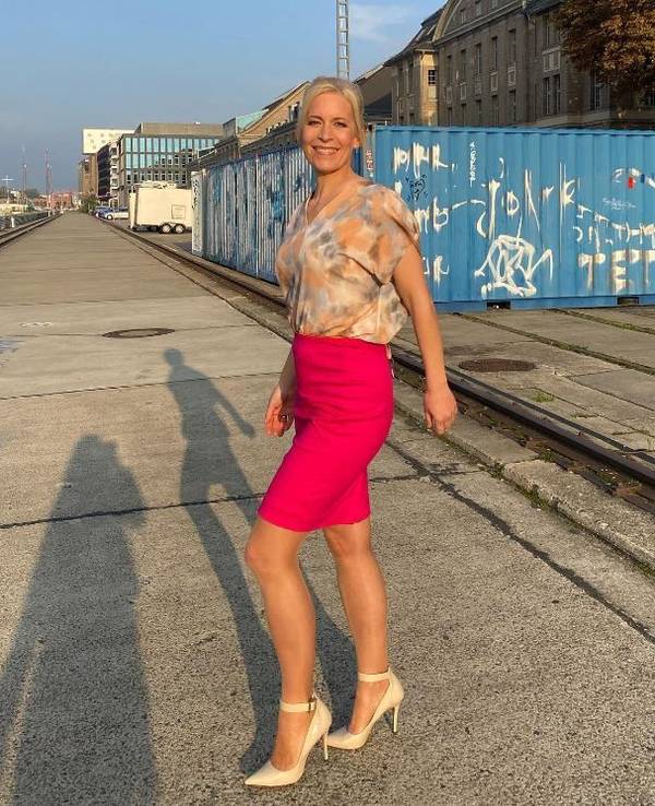 Ina Dietz strahlt in einem bunten Oberteil und einem pinken Rock in die Kamera.