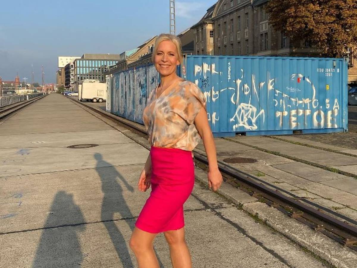 Ina Dietz strahlt in einem bunten Oberteil und einem pinken Rock in die Kamera.