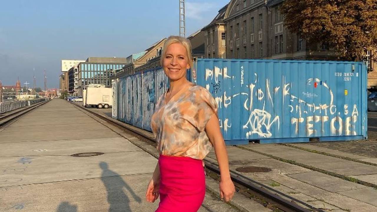 Ina Dietz strahlt in einem bunten Oberteil und einem pinken Rock in die Kamera.