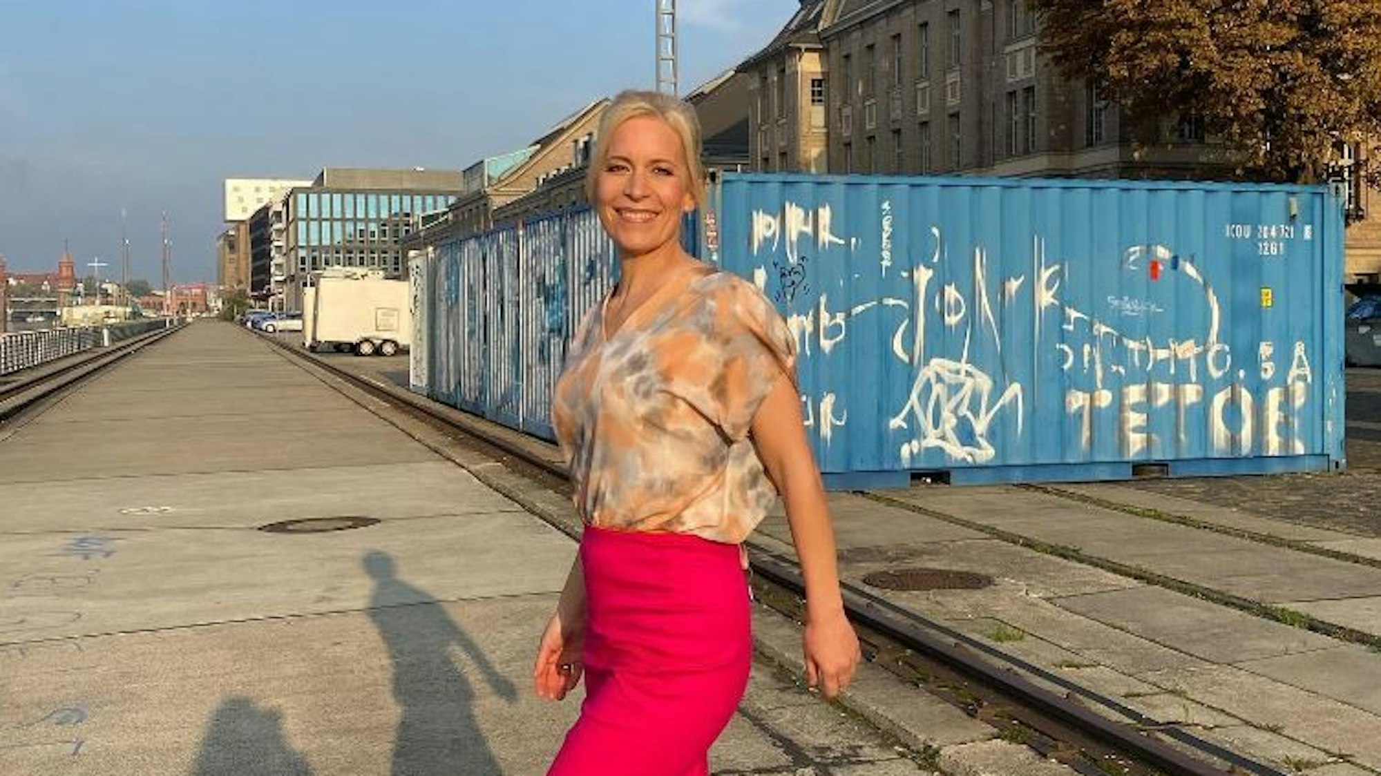Ina Dietz strahlt in einem bunten Oberteil und einem pinken Rock in die Kamera.