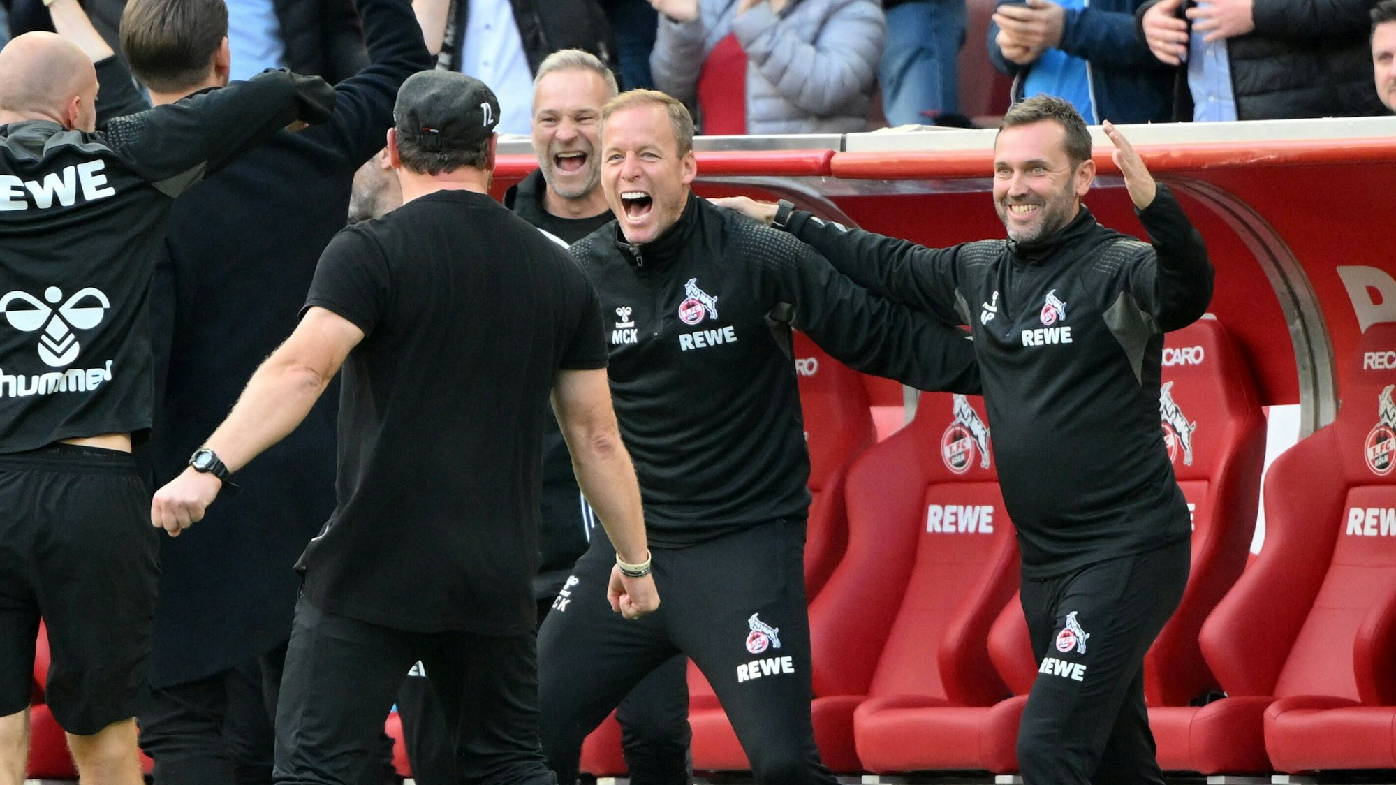 Die FC-Trainer Andre Pawlak, Kevin McKenna, Uwe Gospodarek (v.l.n.r.) jubeln über BVB-Sieg.