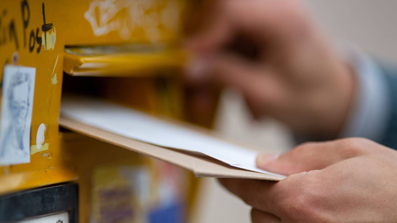 Ein Mann wirft Briefe in einen Briefkasten. Die Aufnahme dient als Symbolfoto.