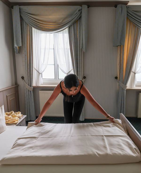 Eine Mitarbeiterin eines Hotels zieht eine Bettdecke in einem Hotelzimmer glatt.