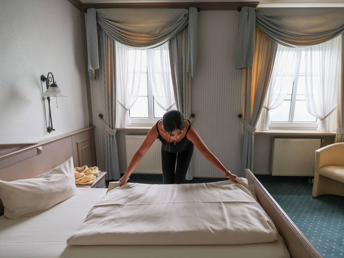 Eine Mitarbeiterin eines Hotels zieht eine Bettdecke in einem Hotelzimmer glatt.