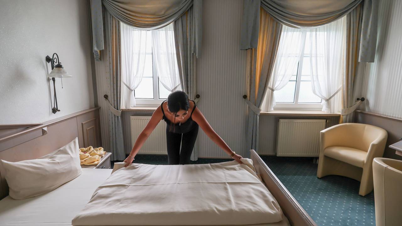Eine Mitarbeiterin eines Hotels zieht eine Bettdecke in einem Hotelzimmer glatt.