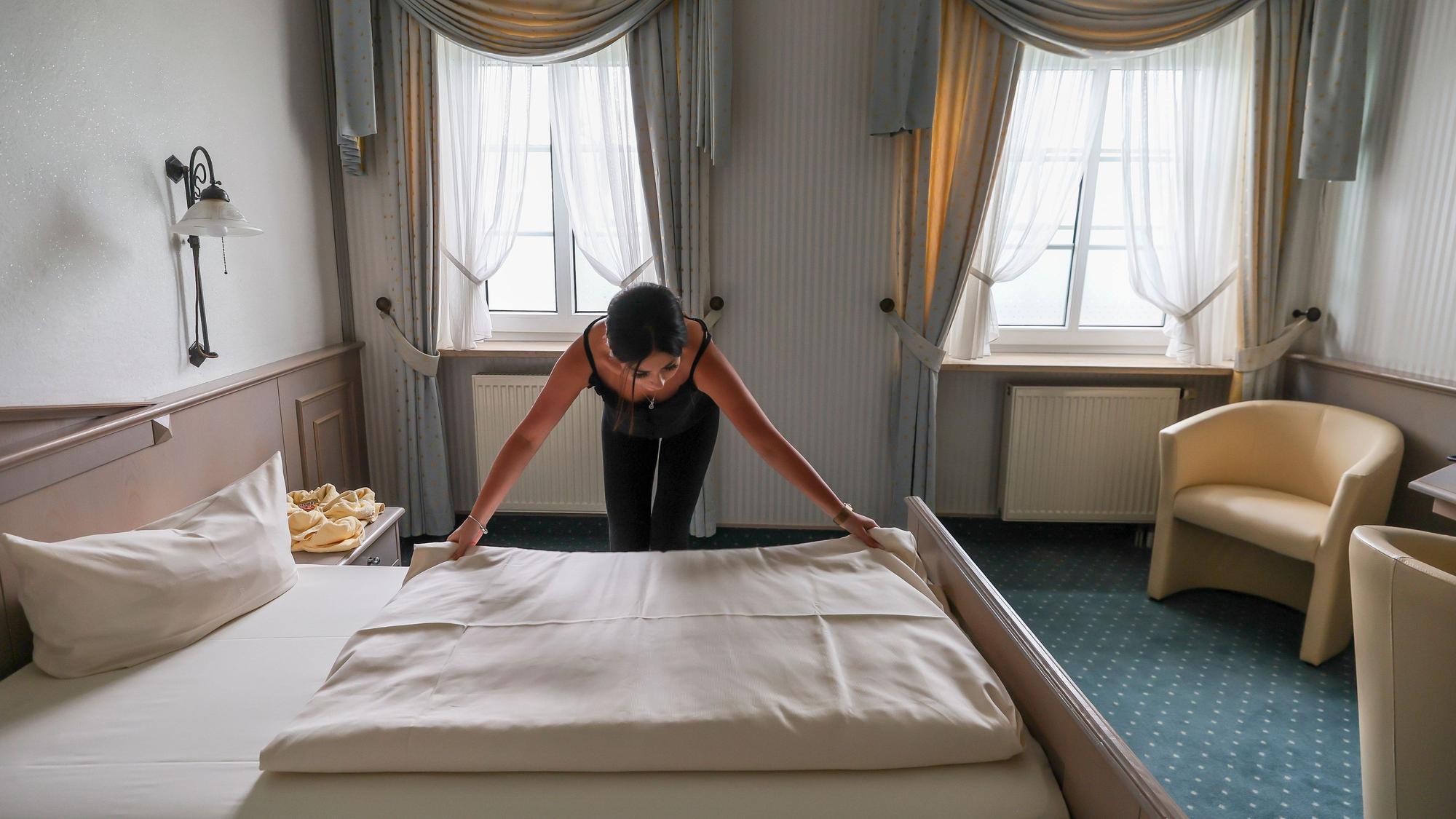 Eine Mitarbeiterin eines Hotels zieht eine Bettdecke in einem Hotelzimmer glatt.