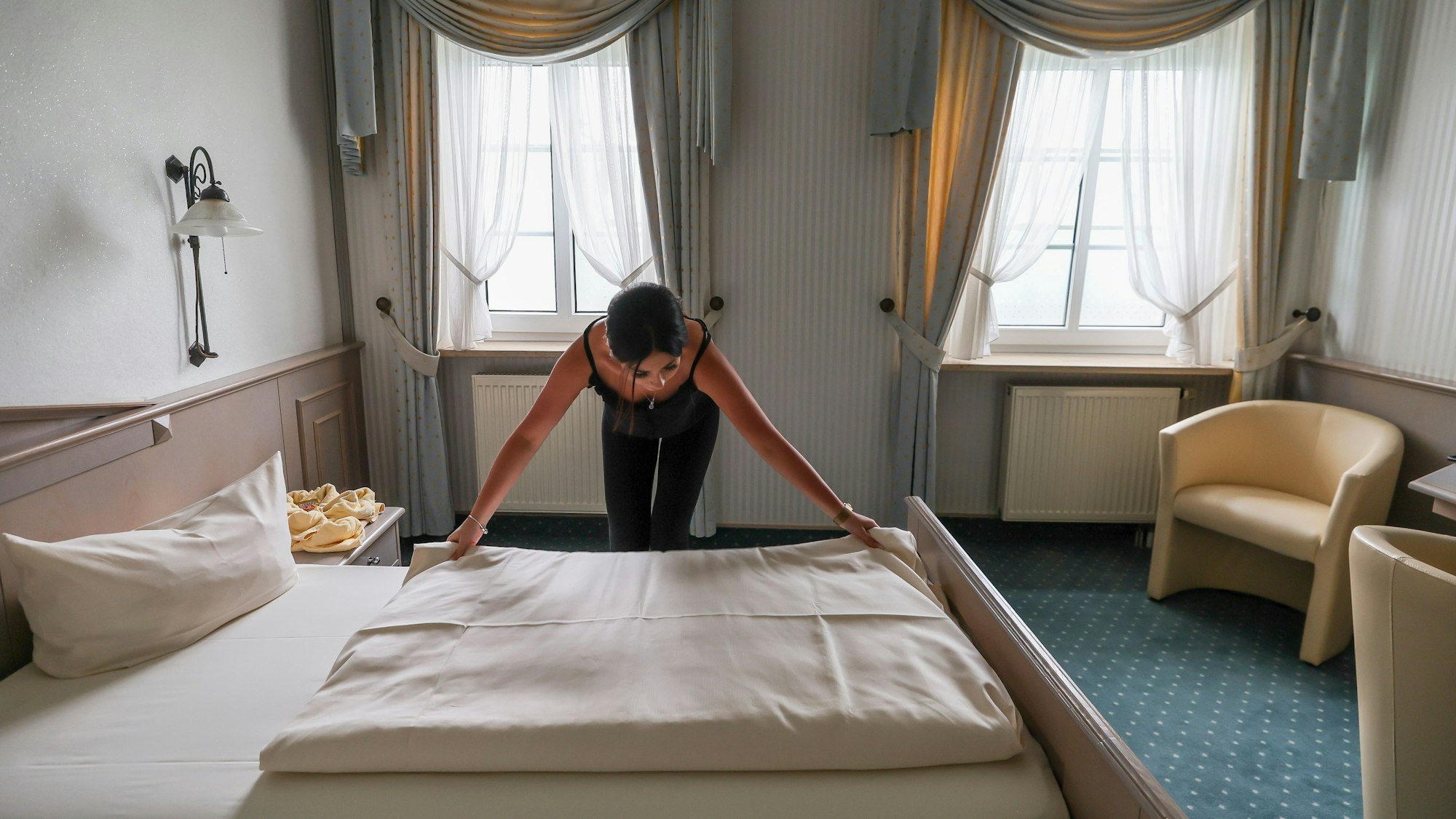 Eine Mitarbeiterin eines Hotels zieht eine Bettdecke in einem Hotelzimmer glatt.