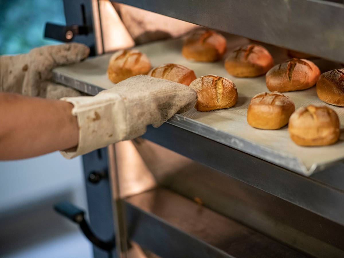 Eine Person schiebt in der Bäcker-Innung Berlin Blech mit Brötchen in den Ofen.