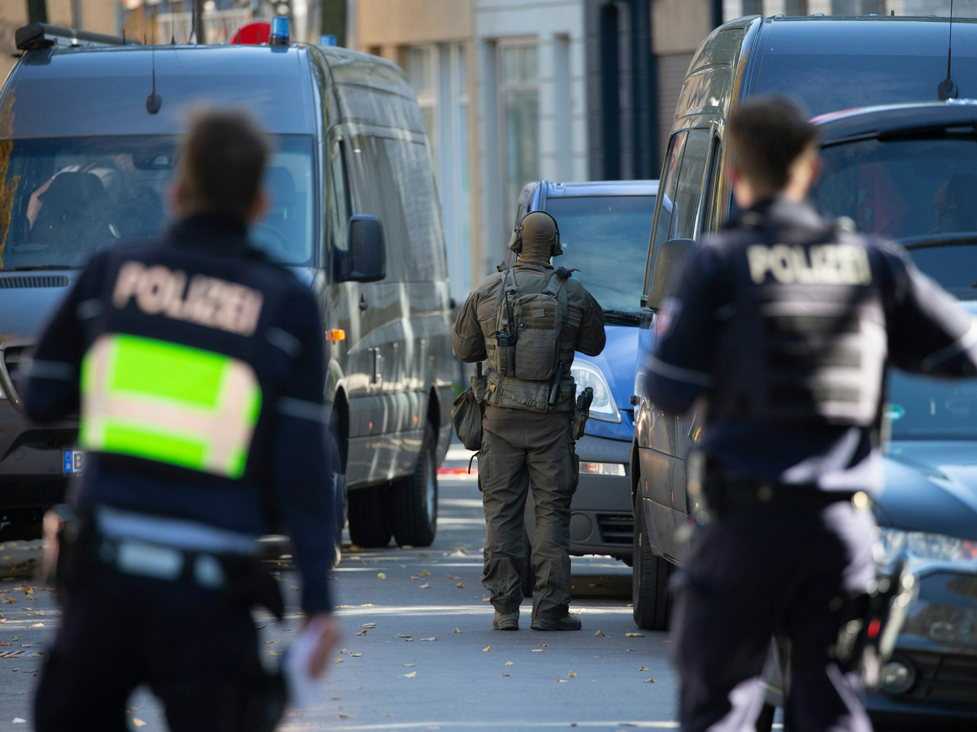 Zwei Polizisten und ein SEK-Beamter stehen zwischen mehreren Fahrzeugen.