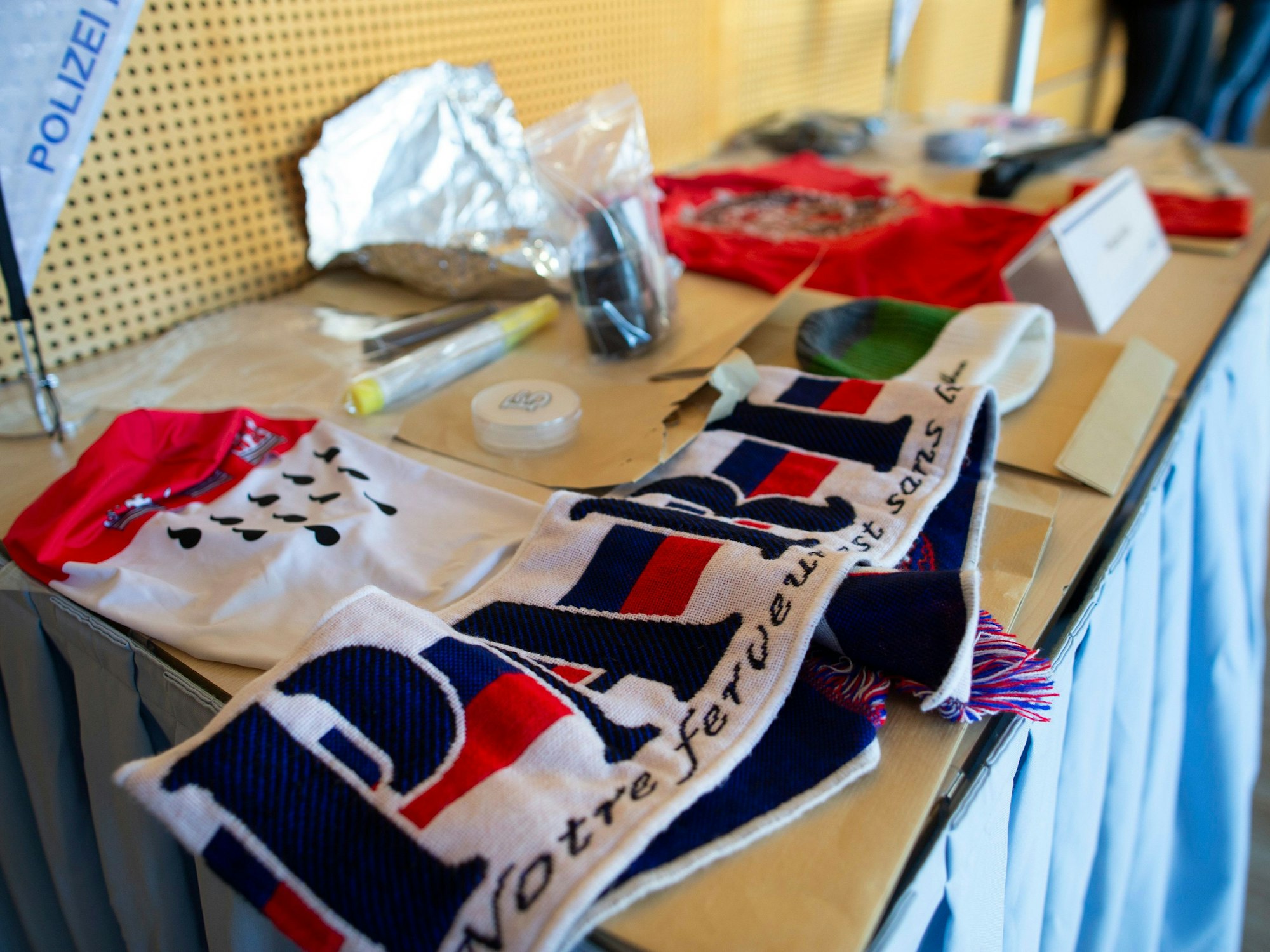 Sichergestellte Gegenstände liegen während einer Pressekonferenz im Polizeipräsidium Köln zum Ergebnis der Hausdurchsuchungen im Zusammenhang mit den Ausschreitungen und Durchsuchungen beim Conference-League-Spiel des 1. FC Köln in Nizza zur Ansicht aus.