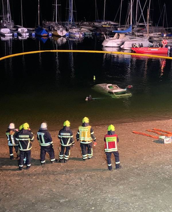 Ein Kleinbus ist im Wasser versunken, mehrere Kräfte der Feuerwehr stehen am Seeufer.